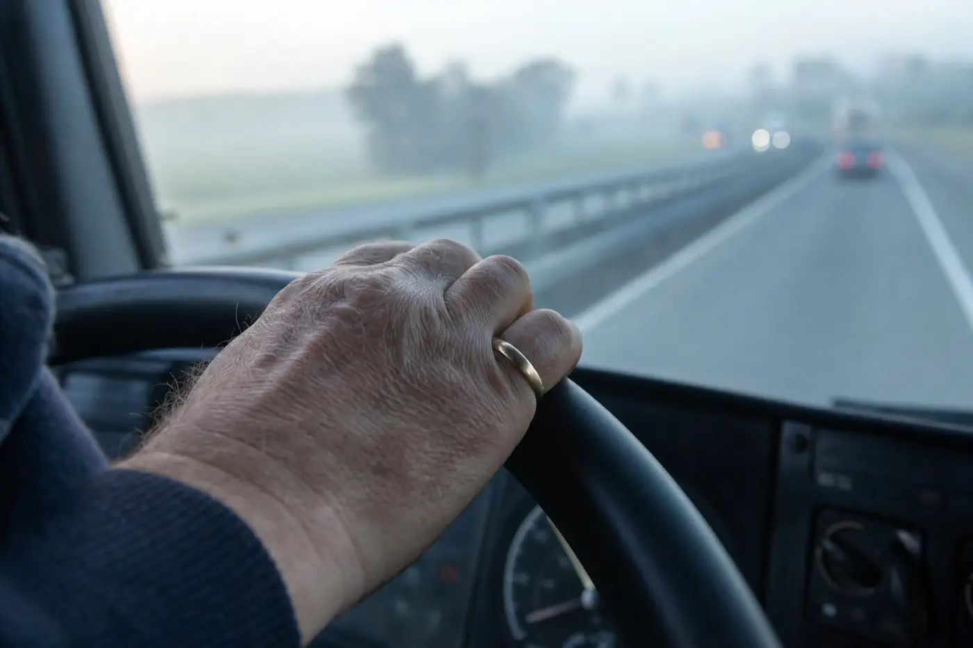 Hand eines Fahrers am Lenkrad eines Lkw, der Ehering ist zur Fingerkuppe gerutscht
