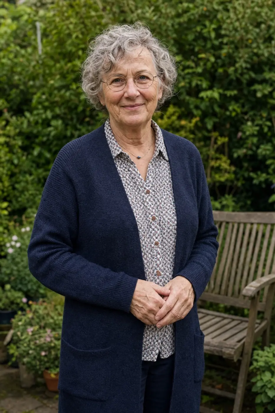 Gudrun, 62, mit grauen Locken und Brille in ihrem Garten.