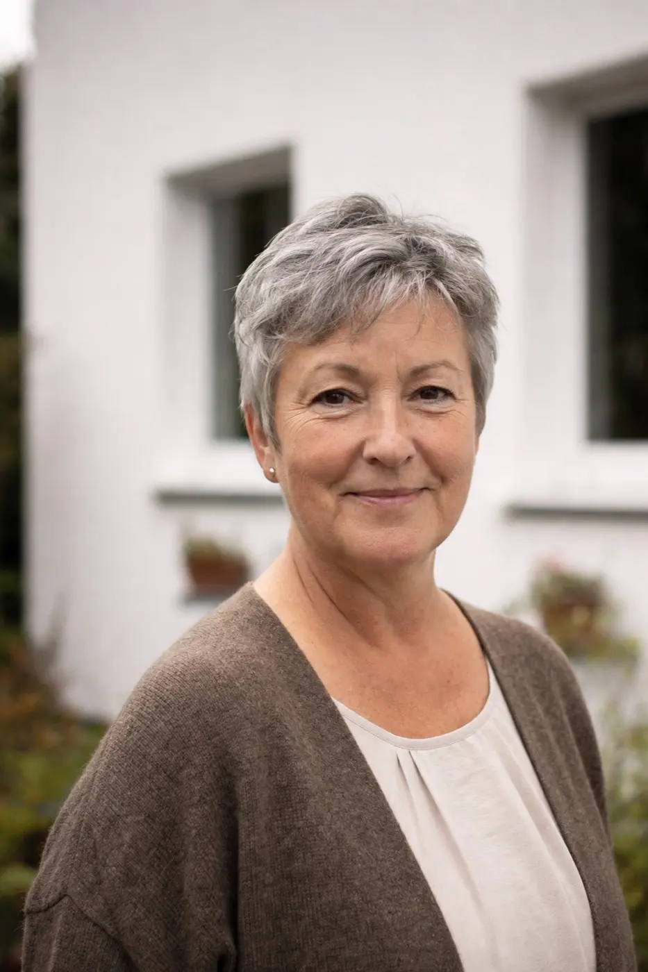 Porträt einer Frau um die 58 mit kurzem grauem Haar vor einer Hausfassade.