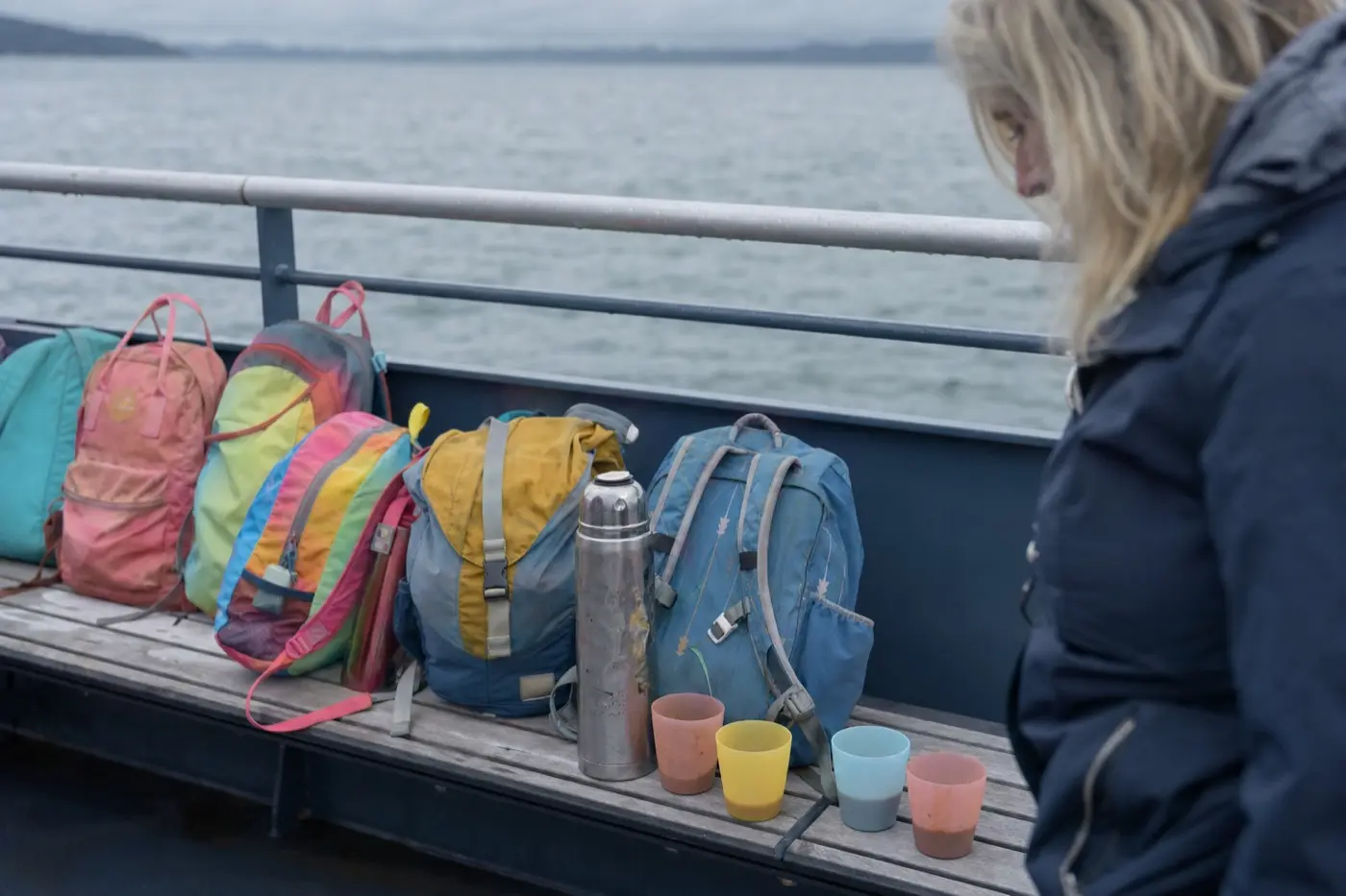 Kinderrucksaecke auf einer Bank an Deck, daneben eine Thermoskanne und Becher mit Kakao.