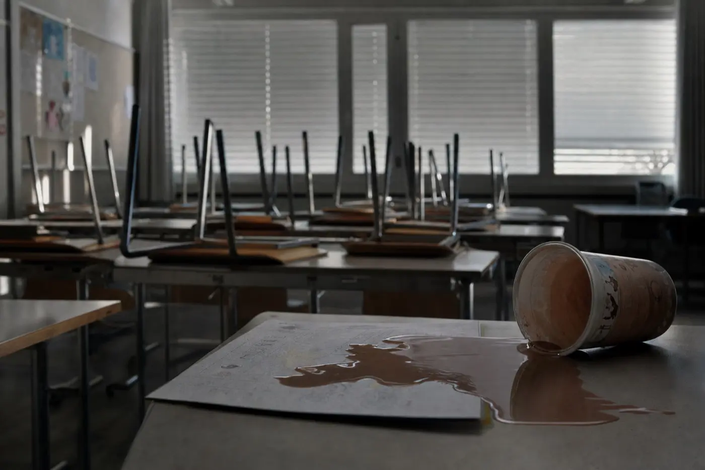 Leeres Klassenzimmer am Morgen, auf einem Tisch ein umgekippter Kakaobecher neben einem Arbeitsblatt.